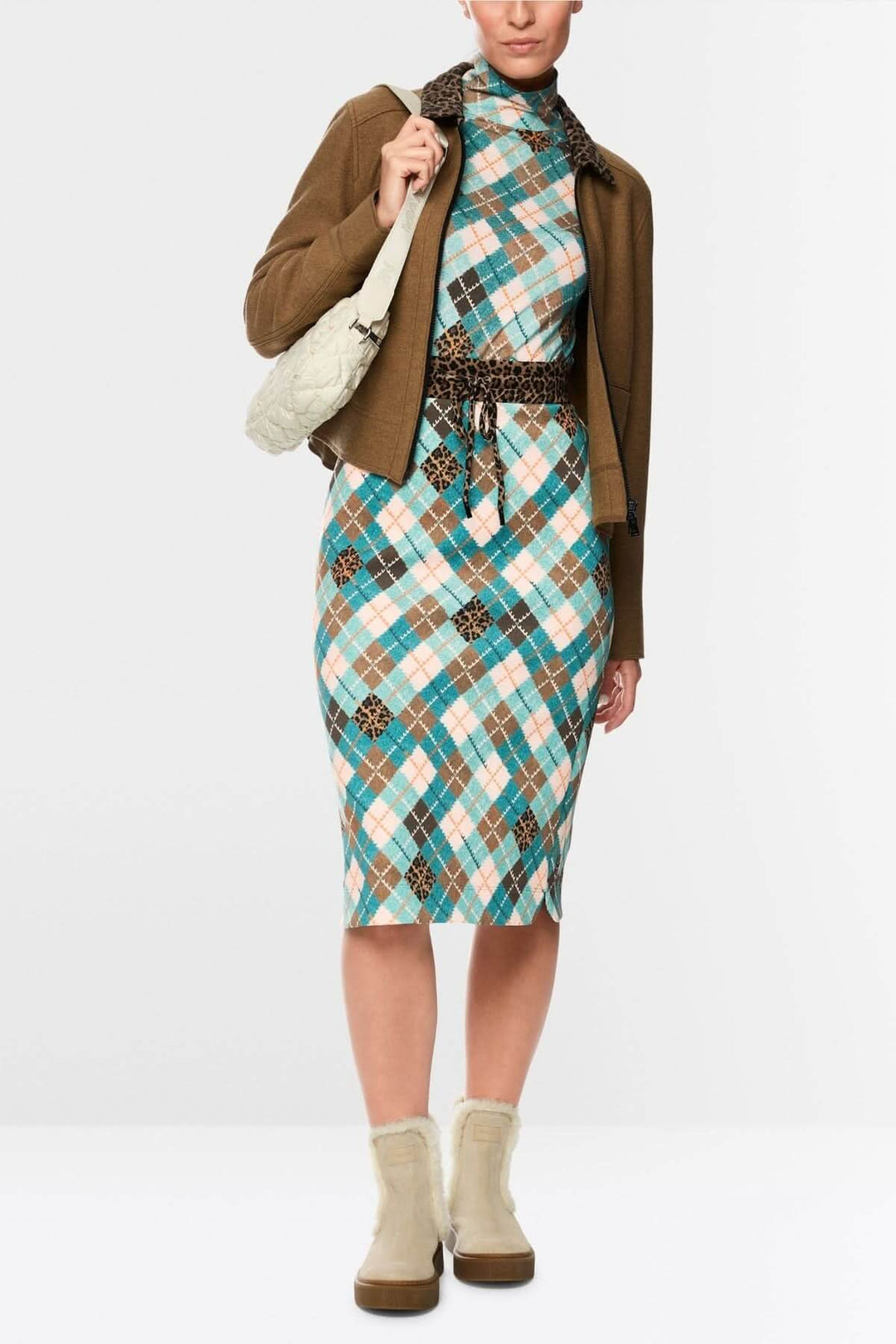 Femme portant un chandail à manches longues en motif argyle multicolore avec col montant, associé à une veste marron et bottines beiges.