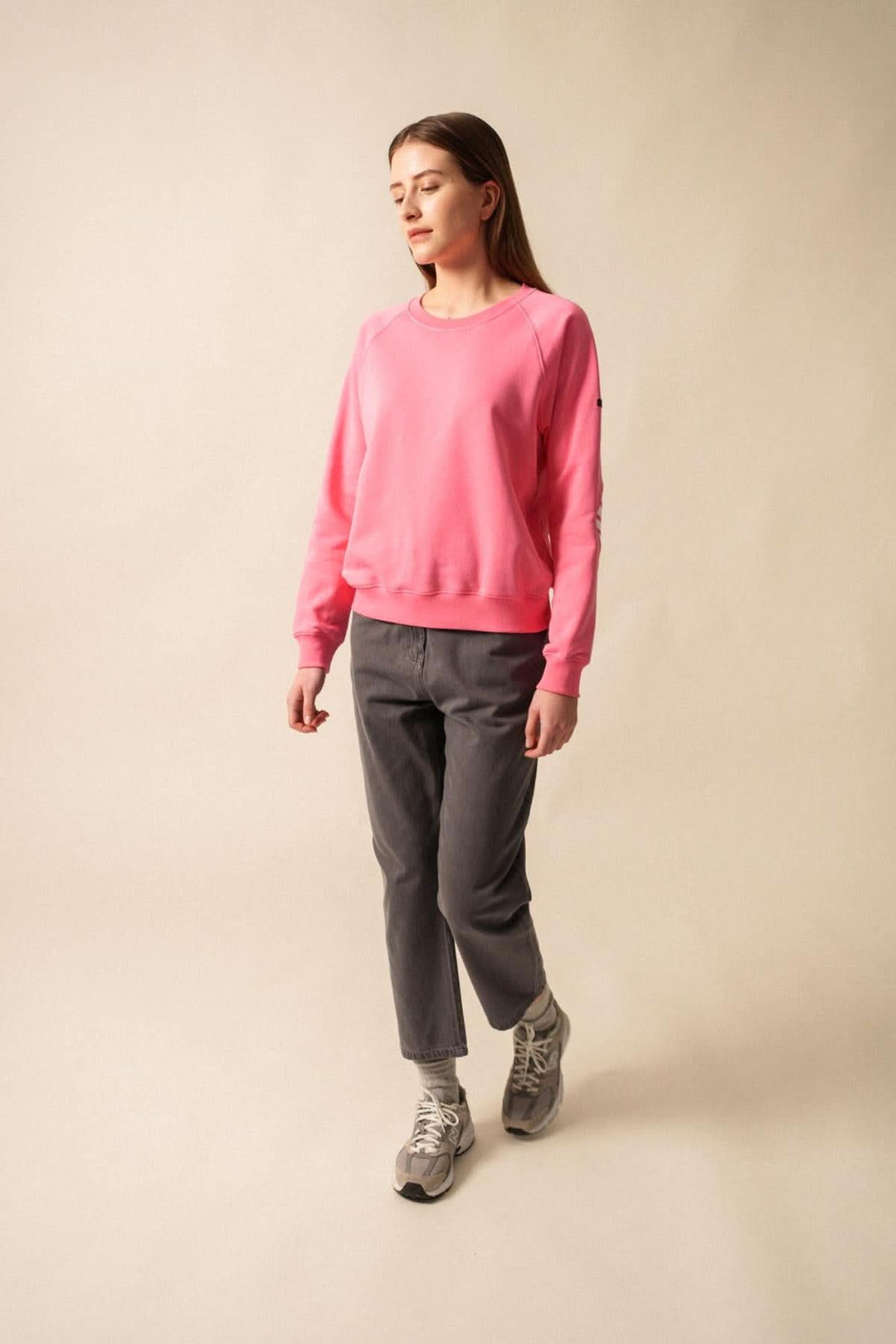 Femme portant un sweat rose en coton, ensemble casual avec pantalon gris, style décontracté.