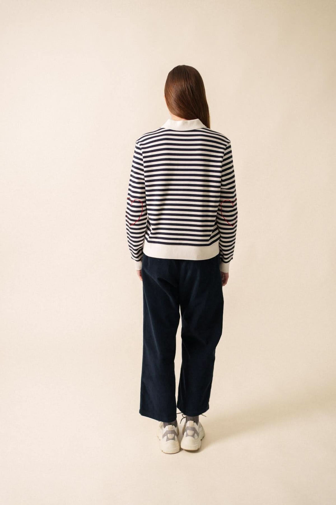 Femme vue de dos portant un chandail polo NINA rayé et un pantalon noir, style décontracté et confortable.
