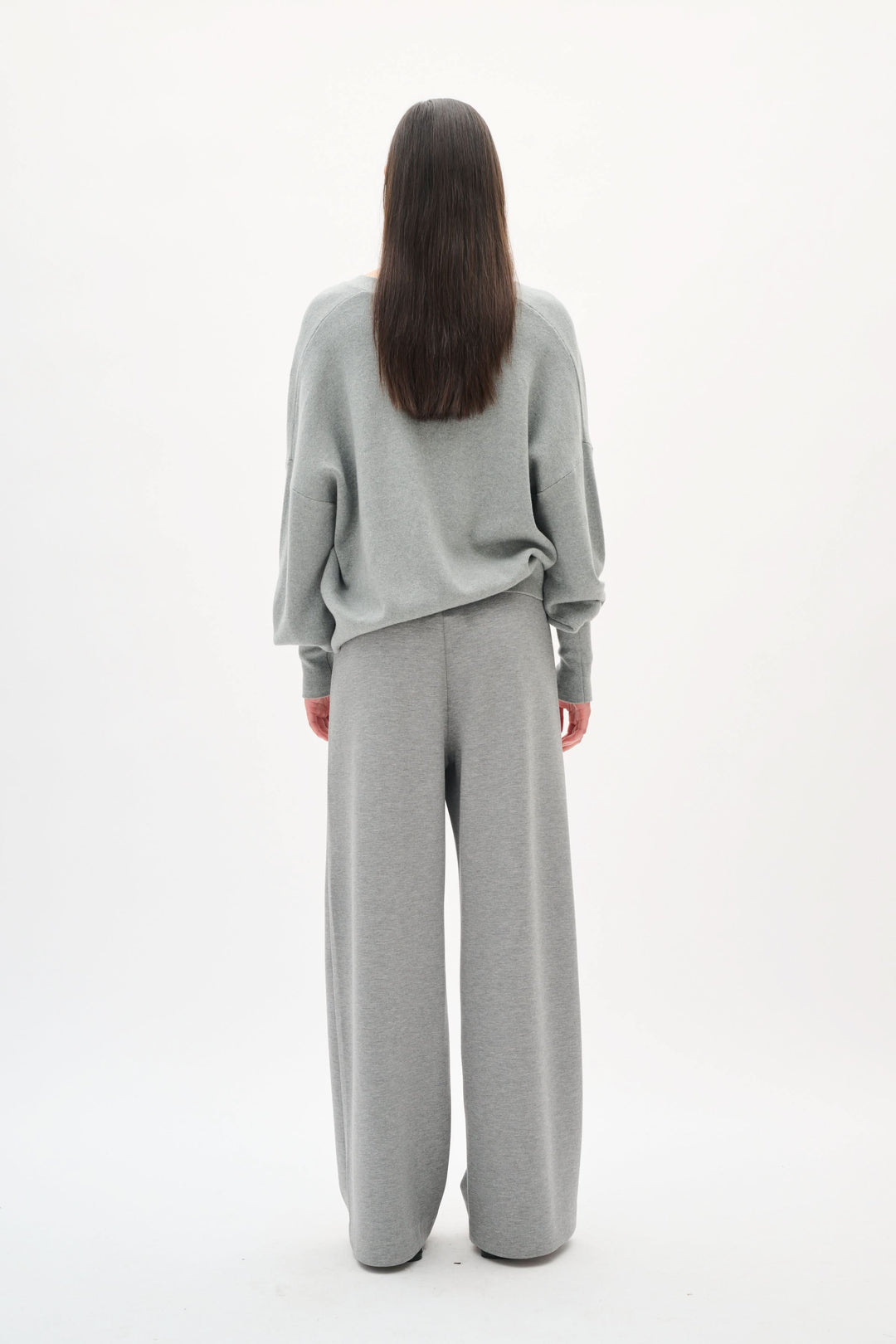 Femme portant un ensemble ample gris, vue de dos, dégageant modernité et confort.