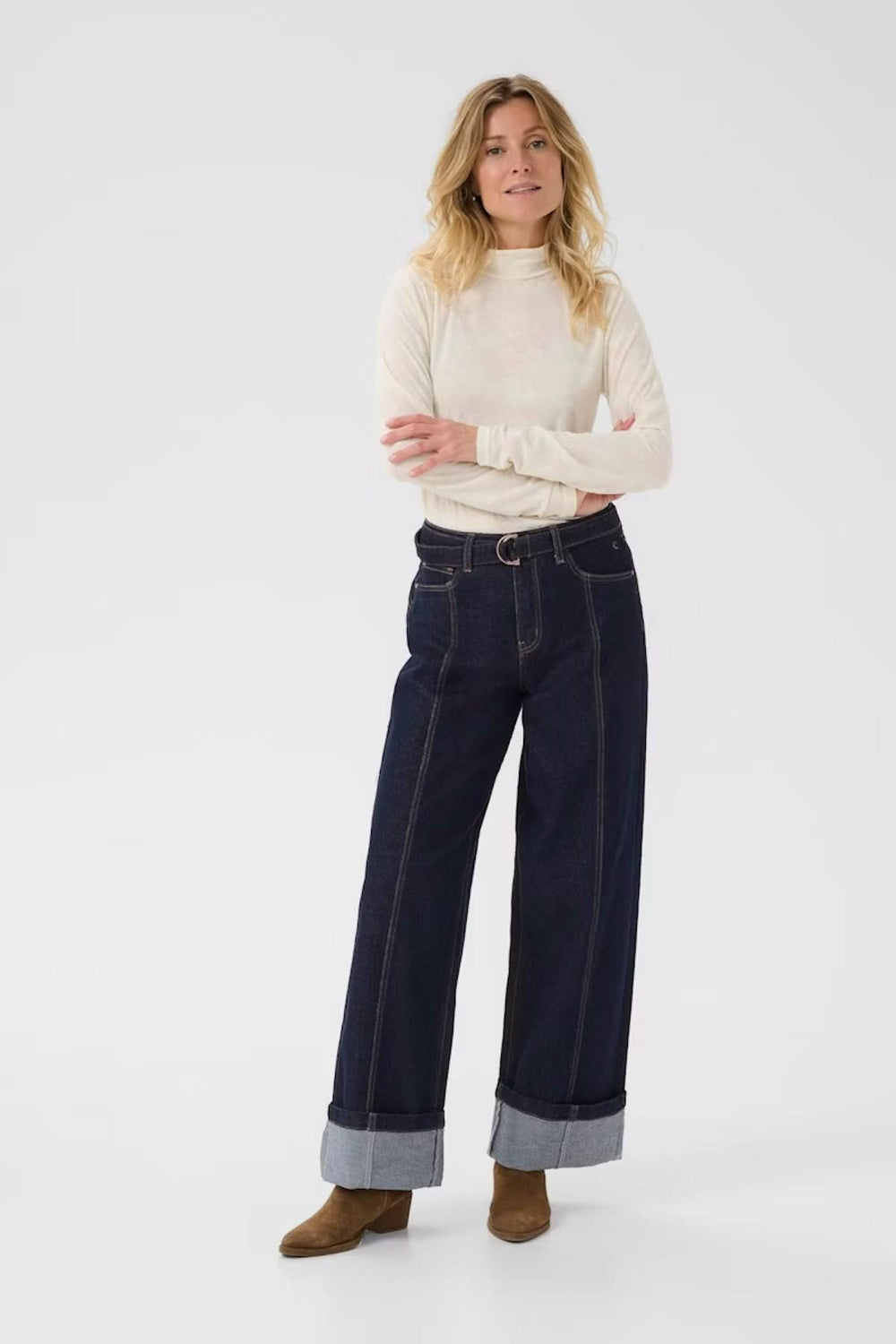 Jean à jambe large avec revers, porté par une femme en pull beige, sur fond blanc.