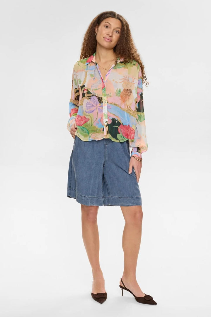 Femme portant une chemise fluide imprimée à manches longues, style artistique et expressif, col classique et manches boutonnées.