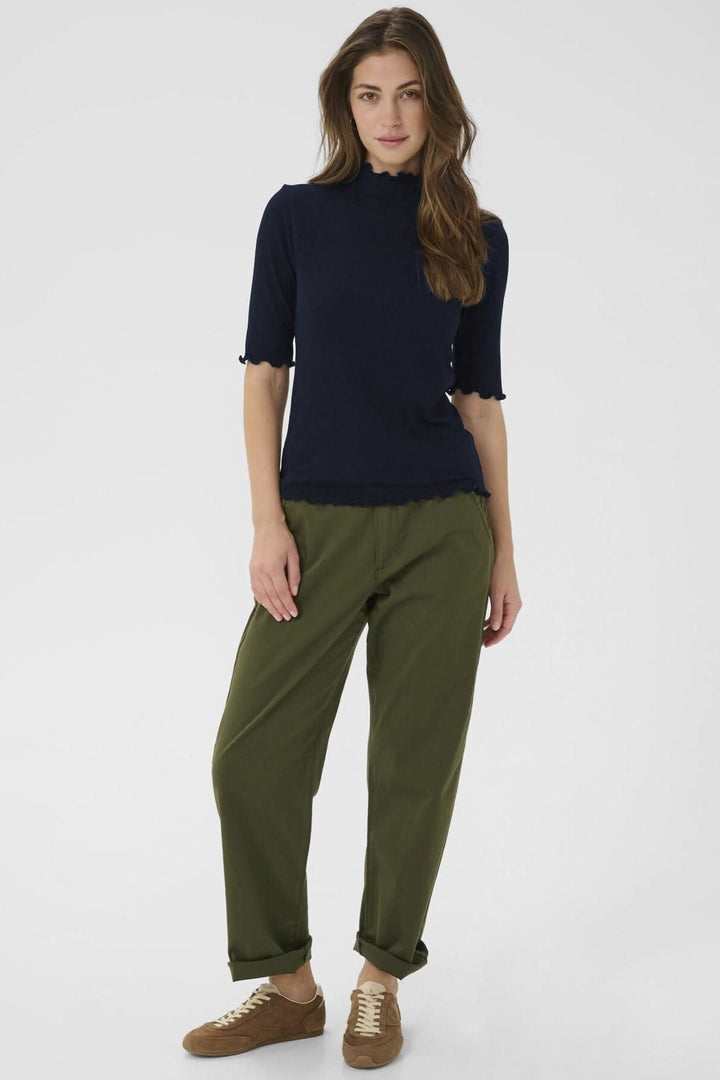 Femme portant le T-shirt Ribba à col montant avec maille côtelée bleu, manches mi-longues, et finitions festonnées élégantes.