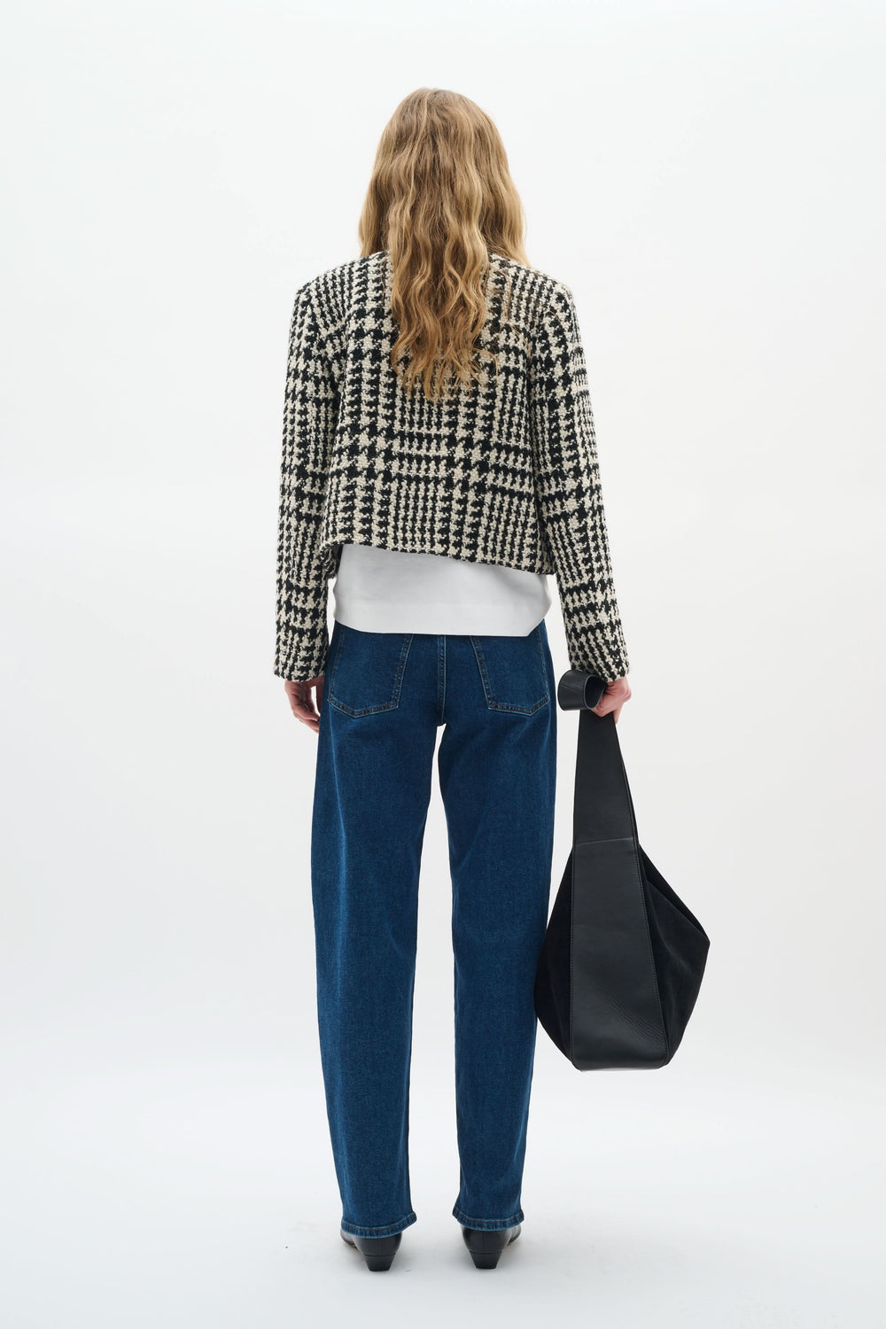 Femme vue de dos portant une veste courte à motif pied-de-poule, un t-shirt blanc et un jean bleu.