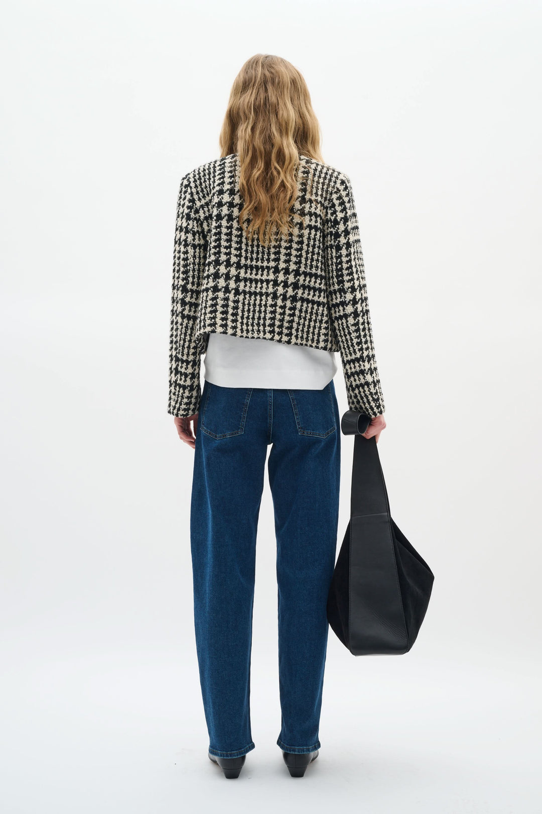 Femme vue de dos portant une veste courte à motif pied-de-poule, un t-shirt blanc et un jean bleu.