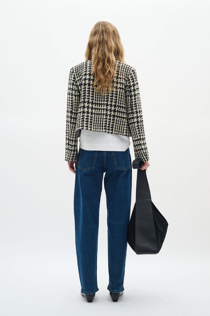 Femme vue de dos portant une veste courte à motif pied-de-poule, un t-shirt blanc et un jean bleu.