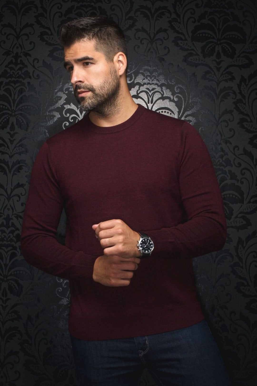 Homme portant un chandail col rond en mérinos marini de couleur bourgogne contre un fond noir élégant.