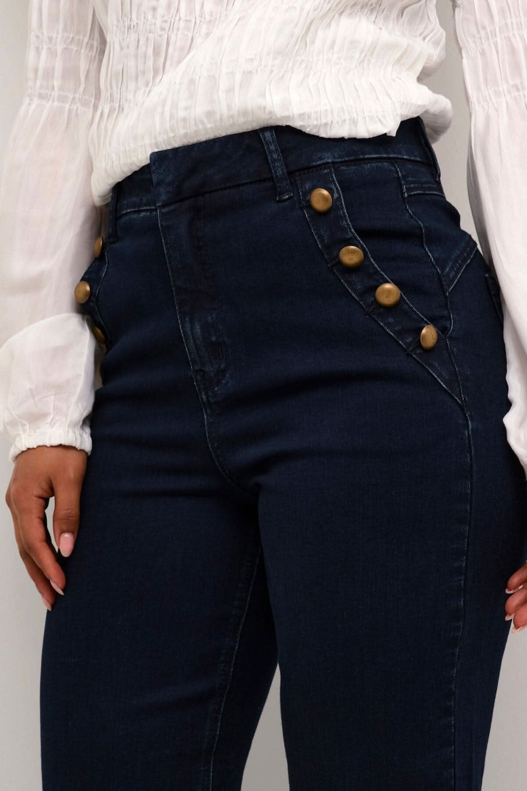 Jean Kanya ajusté avec boutons décoratifs, poches avant et taille haute, sur un modèle avec chemise blanche.