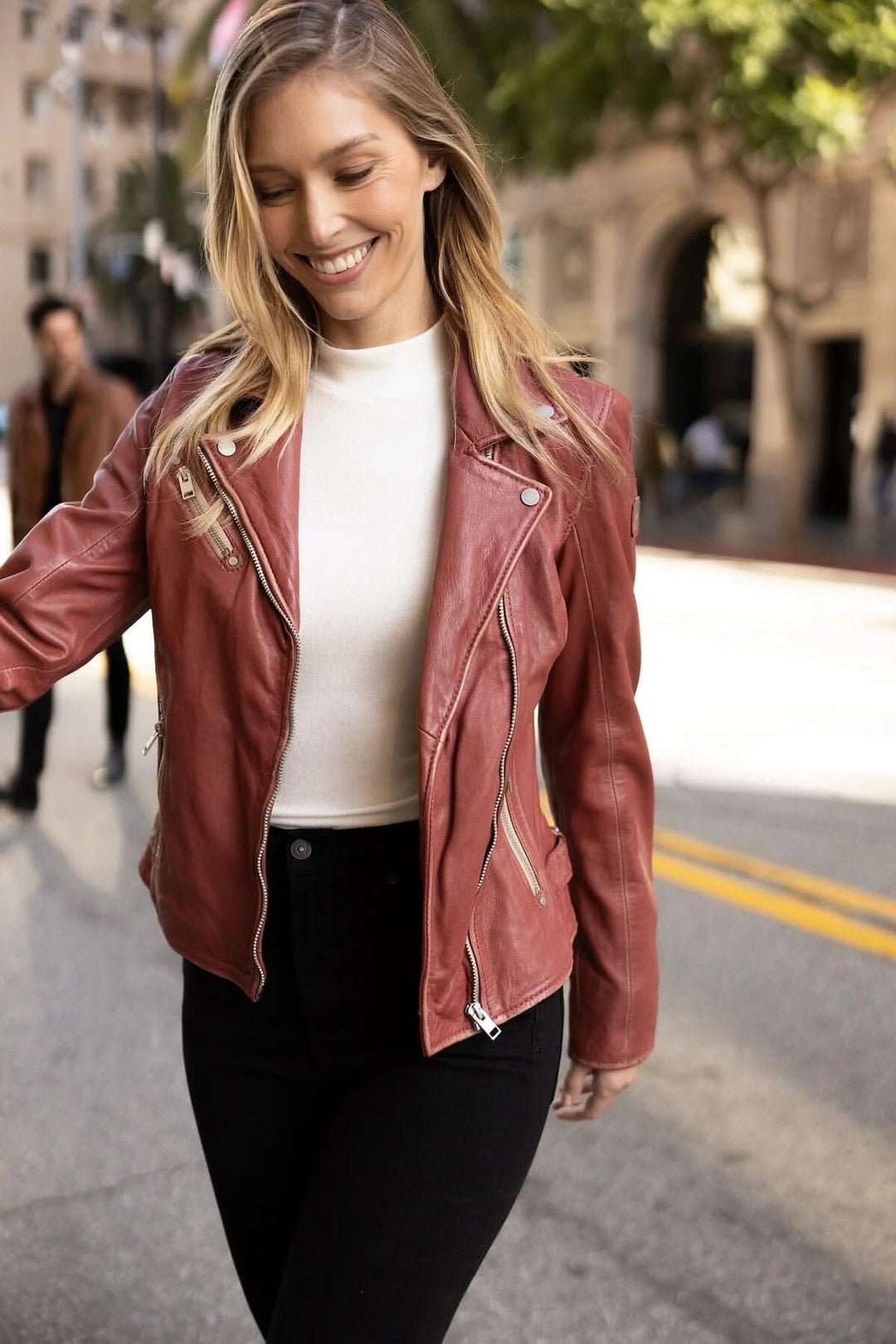 Veste en cuir Sofia, style moto, portée par une femme souriante dans la rue, parfaite pour diverses occasions.