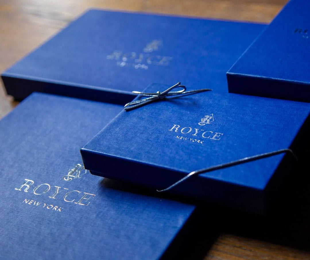 Stylish blue gift boxes from ROYCE New York, featuring elegant gold logo and delicate ribbon detail.